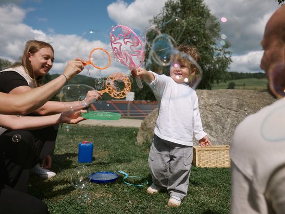 Kleiner Junge spielt zusammen mit den Kinderbetreuerinnen im Schreinerhof mit Seifenblasen