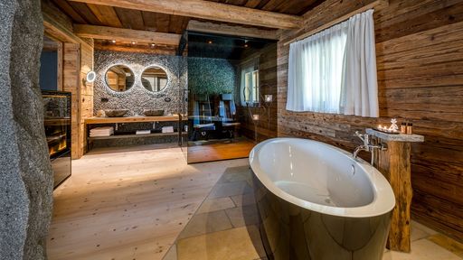 Modernes Badezimmer im Lieblings-Chalet mit zwei Waschbecken, Infrarotstühlen und liebevollen, traditionellen Details aus Holz und Stein.