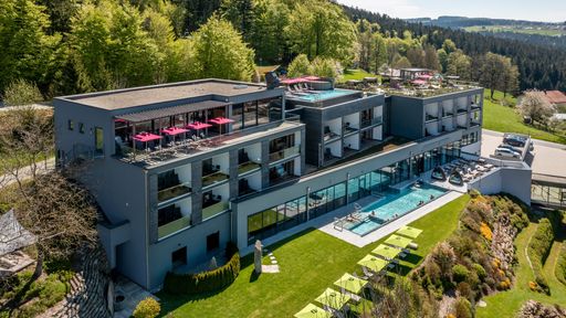 Hüttenhof Wellnesshotel Ansicht im Sommer mit Infinity-Pool, Sky-Pool und Dachgarten umgeben von Natur.
